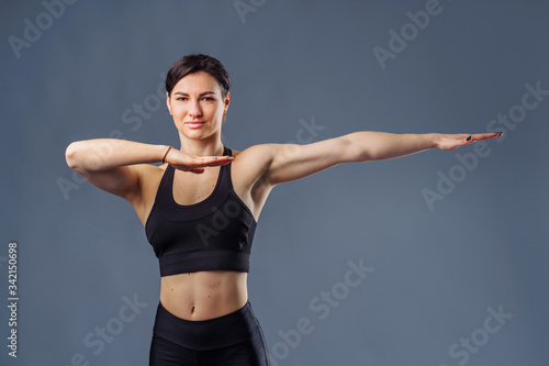 Pumped up sports girl on a grey background in the studio does sports exercises with hands. Smiling and showing her high results by her muscular hands. Fitness for beginners - hands to the side