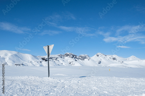 Snow covered road and traffic sign with mountains of Iceland in background