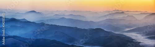 silhouettes of foggy mountains. picturesque mountain peaks at sunrise. © sergnester