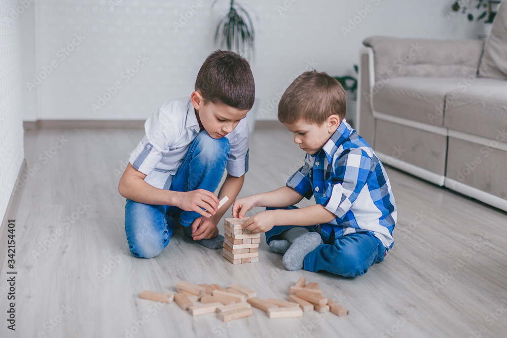 Two brothers boys build a tower of wooden blocks of the house on the floor. Table game. The concept of independent family quarantine, infection, coronavirus, self-isolation. Two brothers boys build a tower of wooden blocks of the house on the floor. Table game. The concept of independent family quarantine, infection, coronavirus, self-isolation.