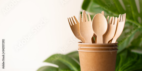 bunner eco friendly disposable kitchenware utensils on white background. wooden forks and spoons in paper cup. and green leaf. ecology, zero waste concept. copyspace.