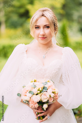 Portrait of a beautiful bride in a wedding dress and a luxurious bouquet of flowers from peony roses, festive makeup and hairstyle