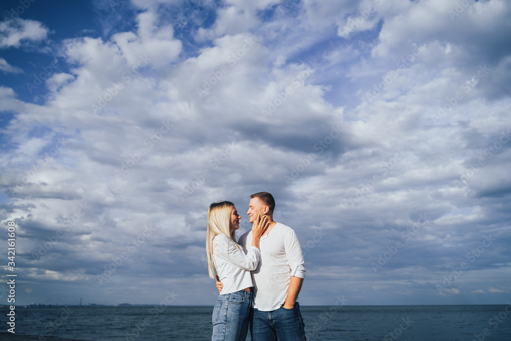 Charming young woman embracing with boyfriend on sea background. Outdoor photo of happy couple standing near ocean. Summer vacation concept. Casual style. Happy together. Outdoor shot