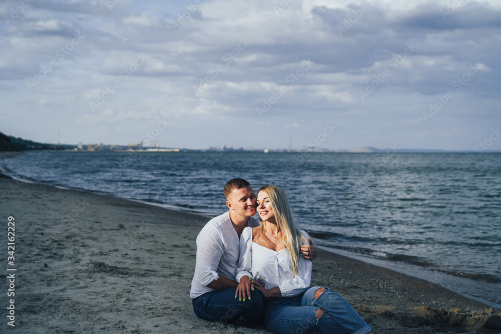 Lifestyle romantic evening for two. Young lovers went on a trip to the sea. Sitting on the sand in the evening sun and hugging, talking, kissing and enjoying the absence of people around. Lifestyle romantic evening for two. Young lovers went on a trip to the sea. Sitting on the sand in the evening sun and hugging, talking, kissing and enjoying the absence of people around.