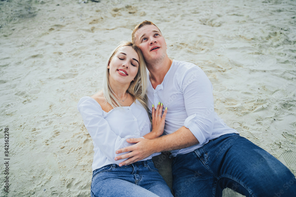 Beautiful happy couple in love lying on a beach on sand in a white shirts are in love smiling. Summer, holidays, vacation and happy people concept Beautiful happy couple in love lying on a beach on sand in a white shirts are in love smiling. Summer, holidays, vacation and happy people concept