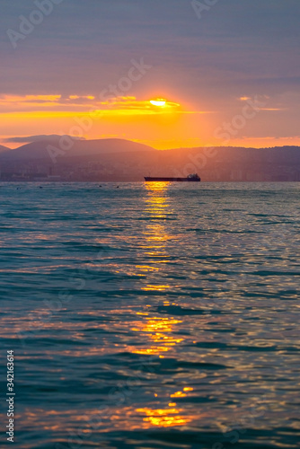 Cargo ship sailing the sea at a golden sunset or sunrise. Ocean shipment across water as the sun sets or rises. Harmony and beauty in nature. Scenic peaceful sea view