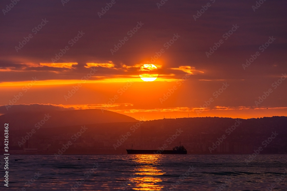 Cargo ship sailing the sea at a golden sunset or sunrise. Ocean shipment across water as the sun sets or rises. Harmony and beauty in nature. Scenic peaceful sea view