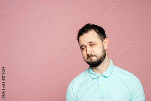 A face of a bearded man on the pink background. A man is sad, confused is ready to cry