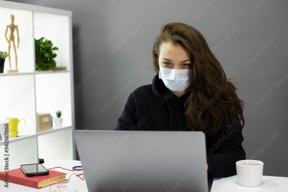 Young sexy beautiful business woman with long hair in medical protective mask working at computer from home office during self-isolation and quarantine. Freelancer works remotely with face mask Young sexy beautiful business woman with long hair in medical protective mask working at computer from home office during self-isolation and quarantine. Freelancer works remotely with face mask
