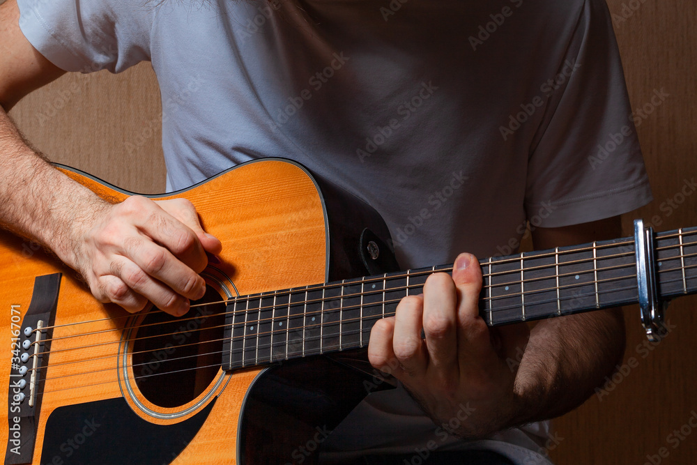 A young European musician in jeans and a white T-shirt plays music on a classical guitar