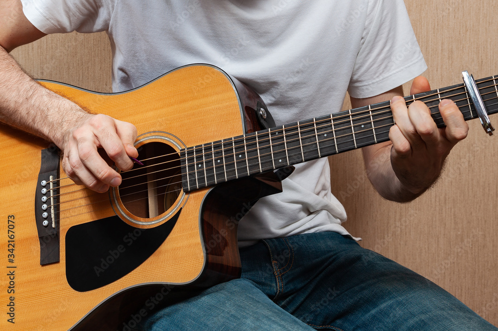 A young European man without a face with jeans and a white T-shirt plays on an acoustic guitar