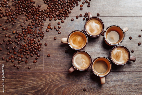 Coffee cup and coffee beans on a wooden background. View from above. Brown background. Close up. Cups with espresso standing on wooden floor, surrounding by roasted beans