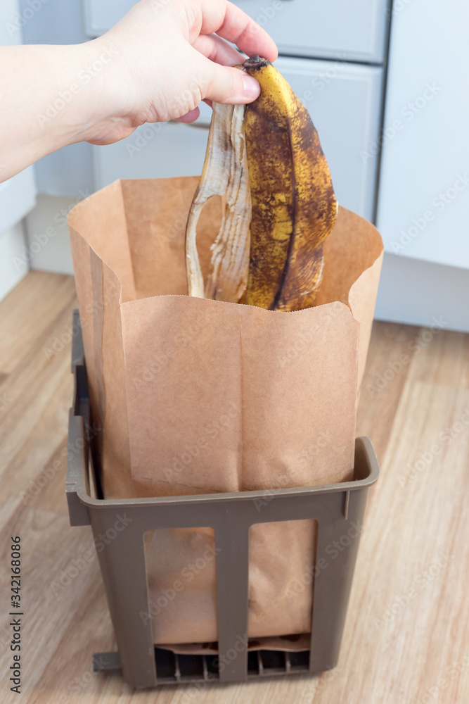 Hand throwing banana peels in a paper bag with food leftovers, garbage  sorting