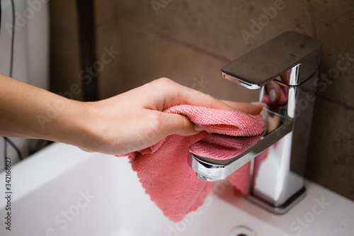 A girl polishes a chrome tap with a microfiber cloth. House and bathroom cleaning. photo