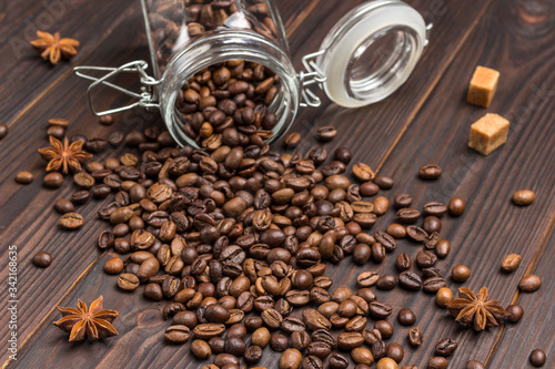 Cup of coffee, coffee beans sprinkled from glass jar on table. Spices star anise and pieces of brown sugar