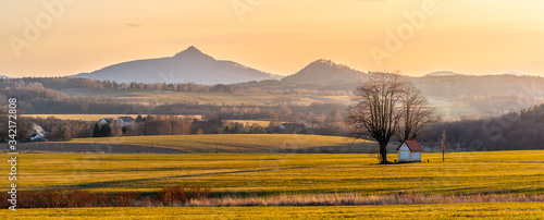 Hilly landscape illuminated by evening sunset. Green grass fields and hills on the horizont. Vivid spring rural countryside. Ralsko Mountain, Czech Republic