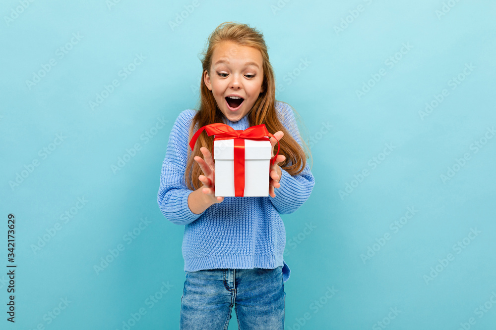 surprised european girl holding a gift on a light blue background surprised european girl holding a gift on a light blue background
