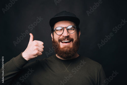 I like it. Portait of a young bearded man showing thumb up or like gesture on black background.