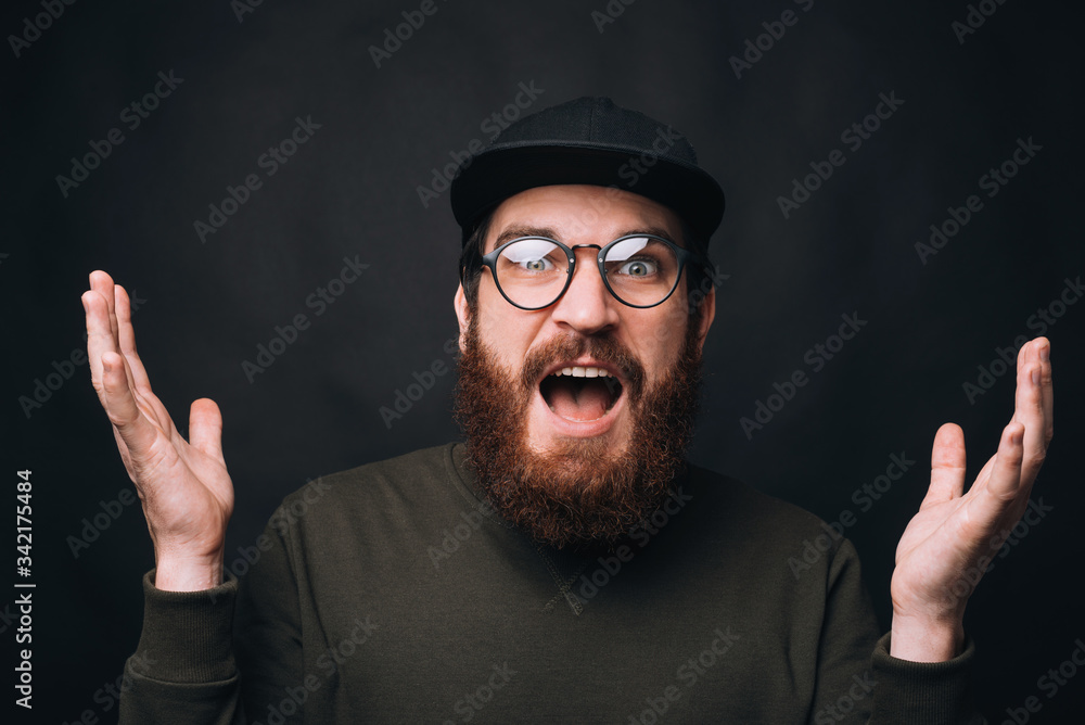 I cannot believe. Shocked bearded man wearing glasses with hands in the air on black background. I cannot believe. Shocked bearded man wearing glasses with hands in the air on black background.