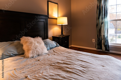 Closeup of bed with decorative fluffy pillow and wooden headboard in bedroom in staging home, house country style