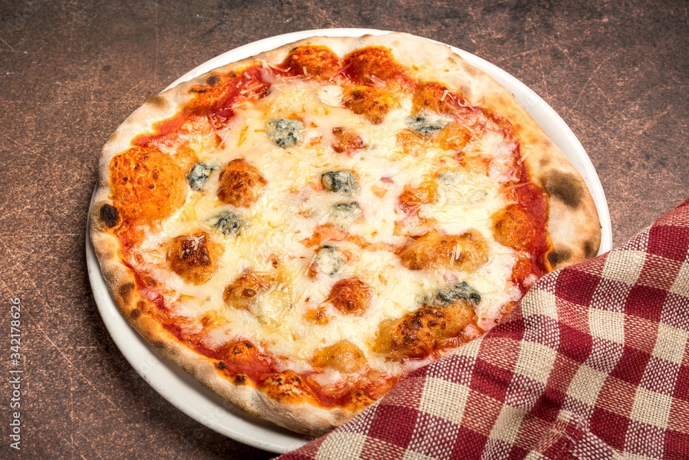 Pizza four cheese on white plate with red checked napkin, top view, brown background. Pizza four cheese on white plate with red checked napkin, top view, brown background.