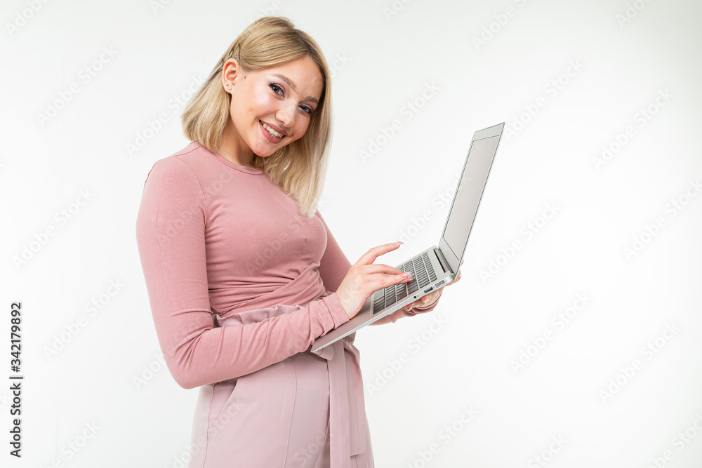 Fototapeta premium charming blonde girl is typing on a laptop computer keyboard while holding it in her hands on a white studio background