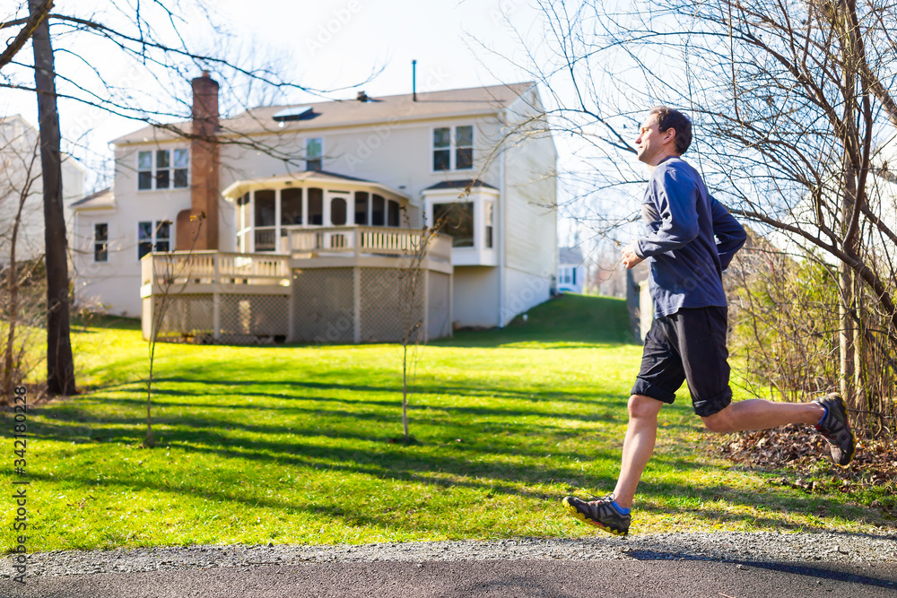 Young man running jogging on trail in residential neighborhood in spring with house backyard in background