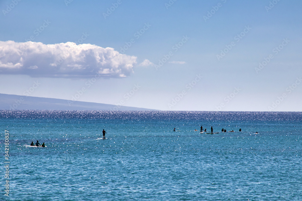 Surfers and stand-up paddlers from a distance on shimmering water on Maui.