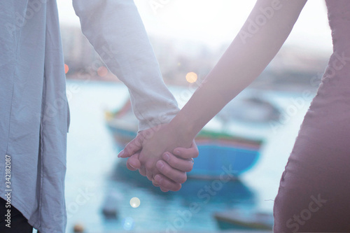 close up of couple holding hands, having date walking in Malta with traditional boat on background,love concept