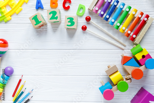 Kids toys: pyramid, wooden blocks, xylophone, train on white wooden background. Top view. Flat lay. Copy space for text 