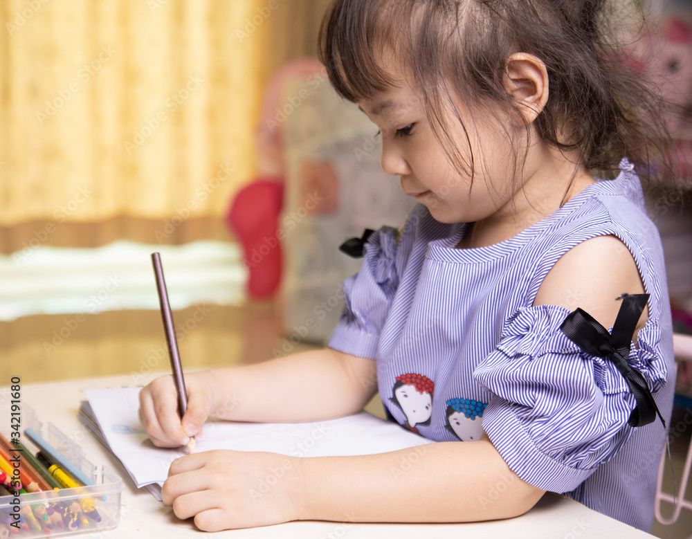 A cute four-year-old Asian girl is sitting and drawing and coloring on her favorite book at home. It develops the skills of preschool children to be ready to study in school and live as they grow up. A cute four-year-old Asian girl is sitting and drawing and coloring on her favorite book at home. It develops the skills of preschool children to be ready to study in school and live as they grow up.