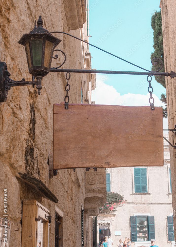 Wooden hanging rectangle sign on the background of vintage homes. ancient city, light colors,blue sky