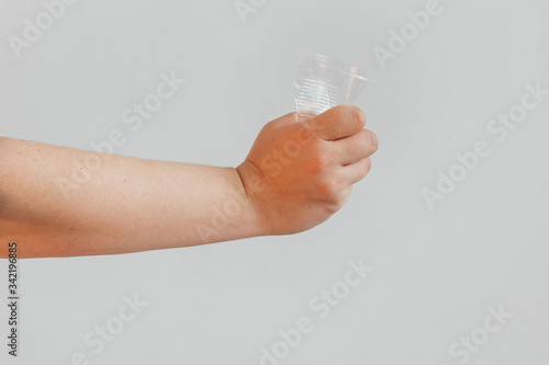 The concept of stopping plastic pollution, global warming, recycling plastic, without plastic. Hand tightly squeezes an empty plastic glass in protest. White background with isolated theme. 