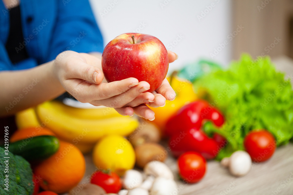 Closeup of woman holding apple in hands on background of vegetables and fruits