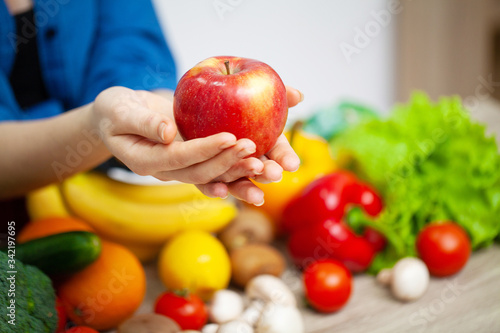Closeup of woman holding apple in hands on background of vegetables and fruits