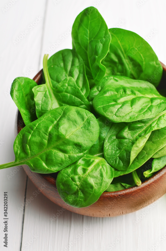 Green spinach leaves in dark wooden bowl on white wooden background. Vegan food lifestyle concept. Green spinach leaves in dark wooden bowl on white wooden background. Vegan food lifestyle concept.