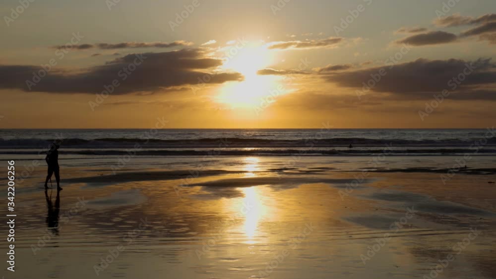 Silhouette of man walking across beach at Sunset at Piha Beach, New Zealand Silhouette of man walking across beach at Sunset at Piha Beach, New Zealand