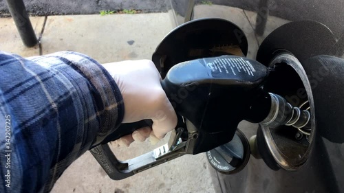 Gas pump toucghing handle with protection gloves while pumping gasoline at gas station during COVID-19 outbreak. 4K photo