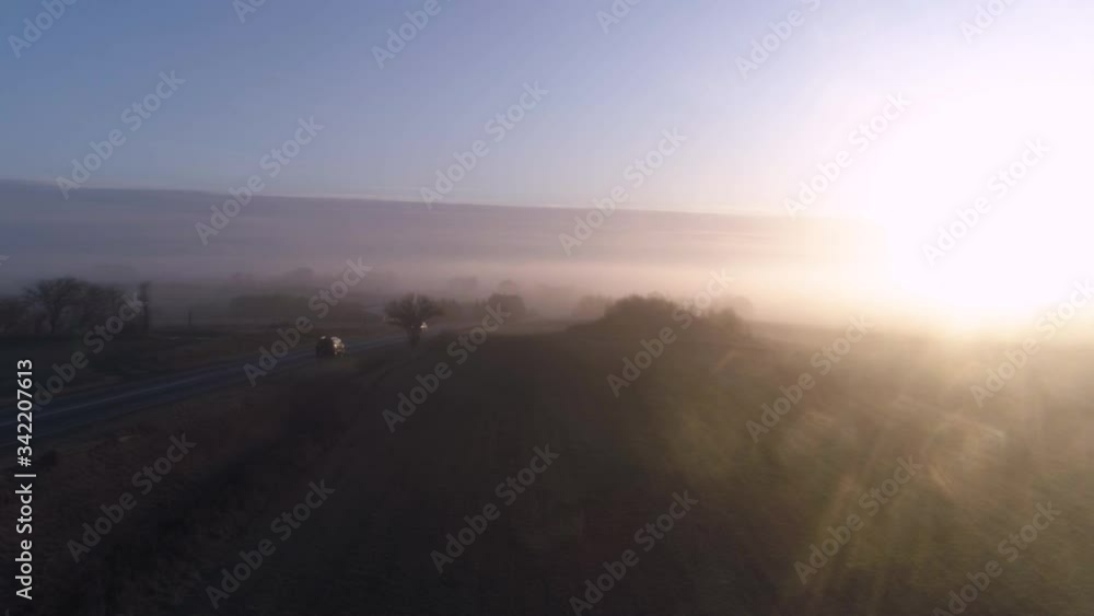 Aerial drone shot of car driving along misty country road at sunrise. Aerial drone shot of car driving along misty country road at sunrise.