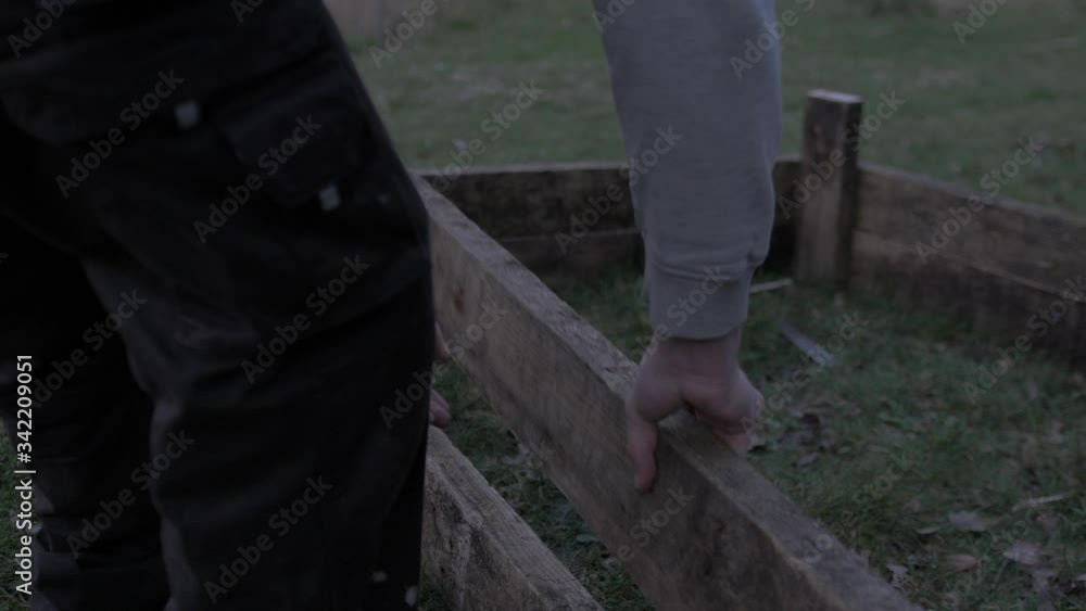 Young man wearing hoodie placing plank building raised garden bed at dusk