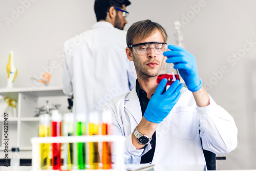 Professional two scientist man research and working doing a chemical experiment while making analyzing and mixing  liquid in test tube.Young science man dropping sample chemical on glass at laboratory