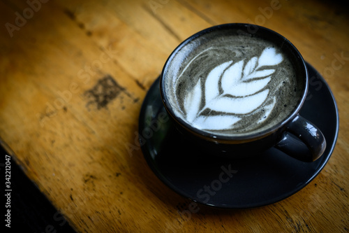 A cup of Goth Latte or Charcoal Latte on wooden table (Focus on coffee surface). The black colour is caused by adding activated charcoal to espresso and then adding milk.