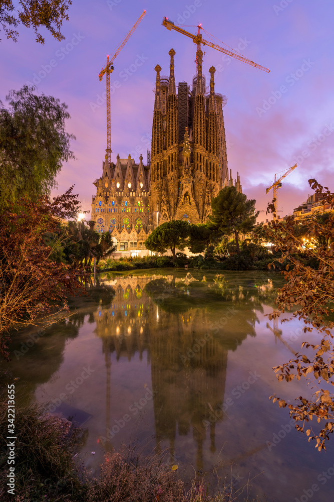 Sagrada Familia - A vertical colorful sunset view of the east Nativity facade of The Basílica de la Sagrada Família, reflected in a small pond. Barcelona, Catalonia, Spain. Sagrada Familia - A vertical colorful sunset view of the east Nativity facade of The Basílica de la Sagrada Família, reflected in a small pond. Barcelona, Catalonia, Spain.
