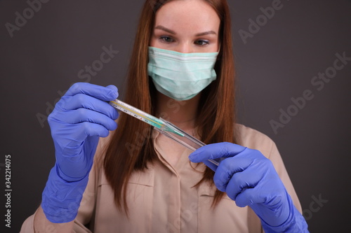 Woman in protective mask reads her temperature on a thermometer.