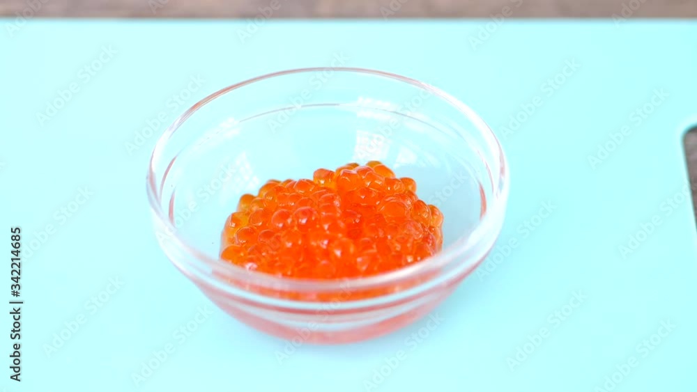 Filling Small Clear Bowl On The Chopping Board With Nutritious Red Caviar - Closeup Shot Filling Small Clear Bowl On The Chopping Board With Nutritious Red Caviar - Closeup Shot