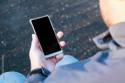 mockup sitting man's hand holding a white mobile phone with a blank screen outdoors