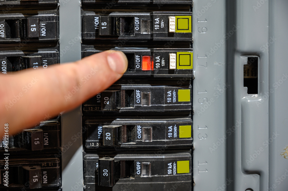 Foto Stock Finger resetting a tripped breaker in residential house electric box Adobe Stock