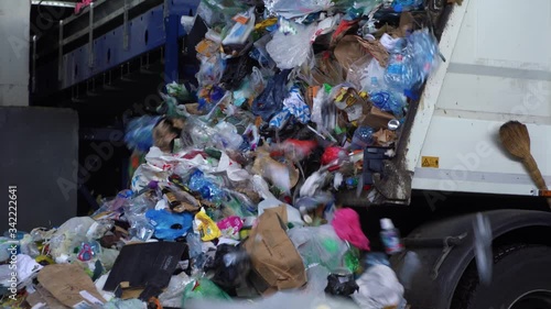 A DUMP TRUCK unloads a massive pile of unsorted garbage at a landfill. Trash spills out onto the ground in a chaotic heap.