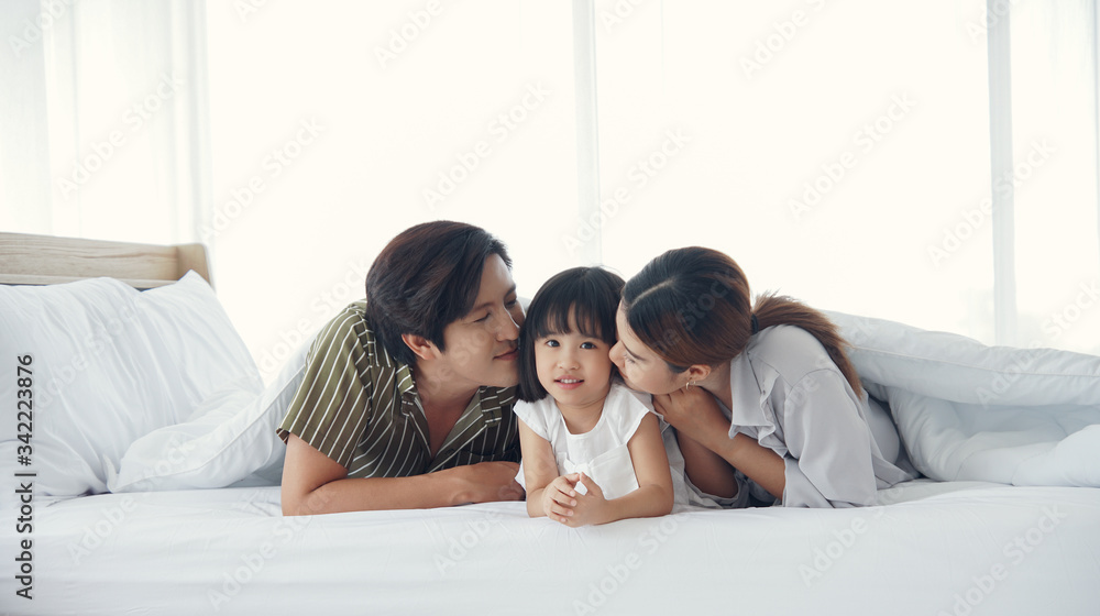 Asian Parents lying on bed under blanket and kissing their little daughter on both cheeks. family portrait. Asian Parents lying on bed under blanket and kissing their little daughter on both cheeks. family portrait.