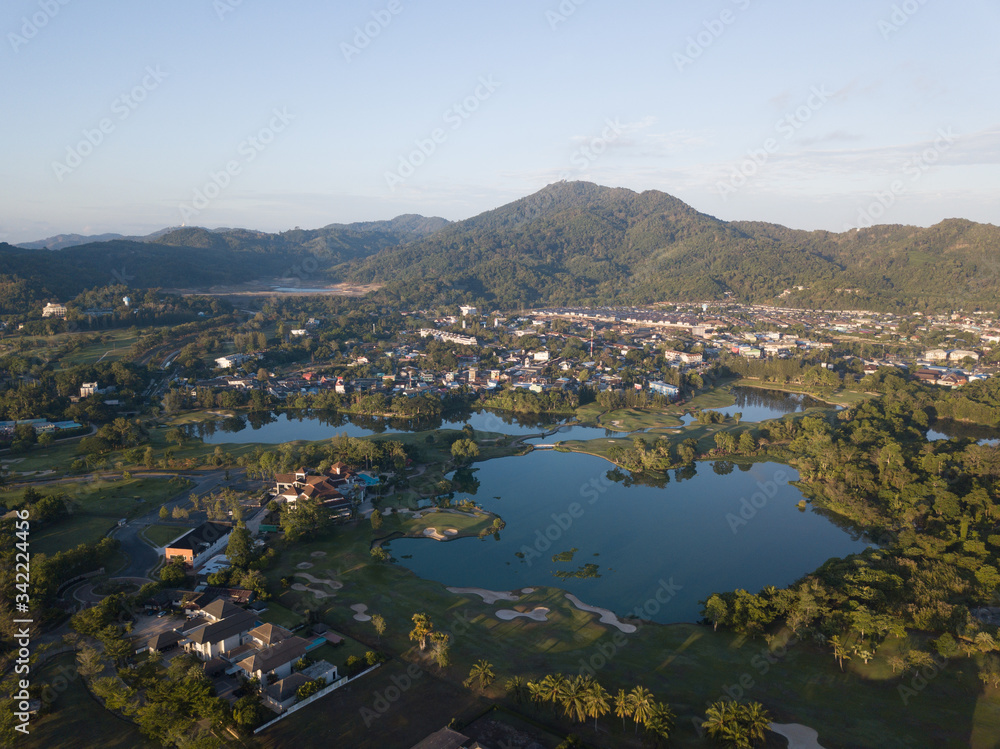 Beautiful lake located on a golf course surrounded by houses and mountains at dawn, photo from a drone. In the lake the reflection of the sky. Great background for travel and golf advertising.
